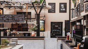 A bar area with a chalkboard menu, a coffee machine, and a sign that reads 'HOME HOTEL VICTORIA'.