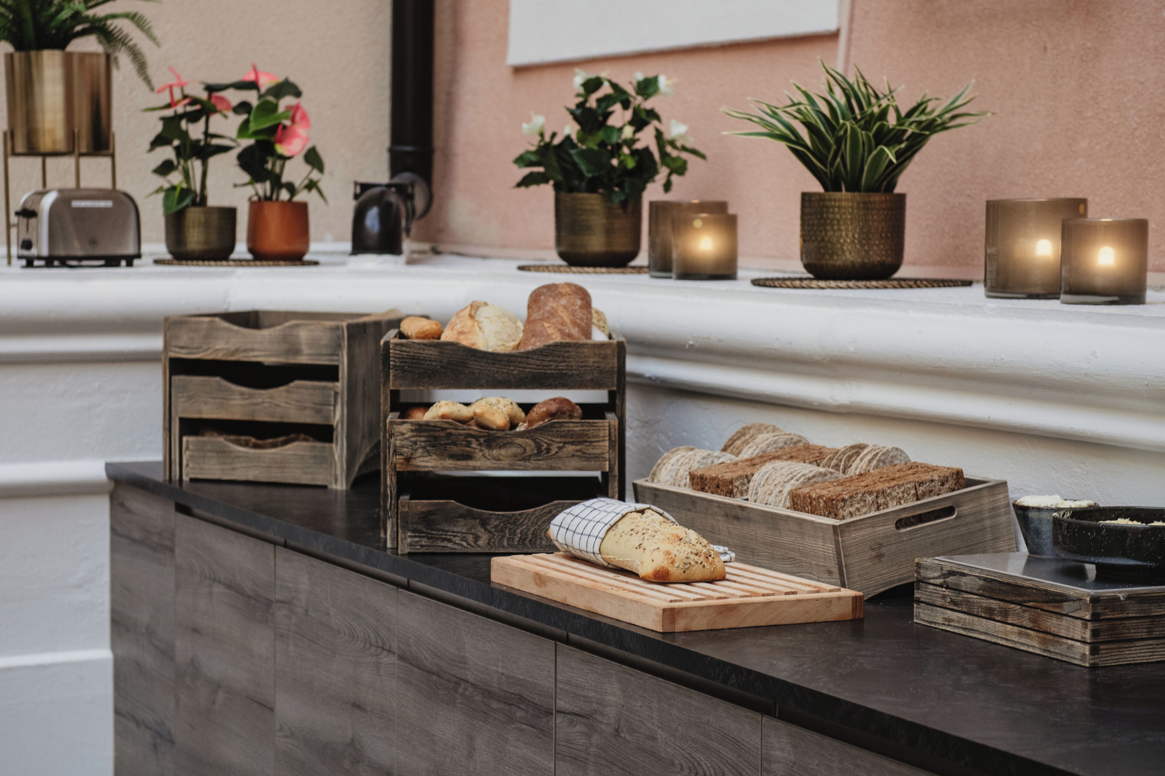 Un plan de travail de cuisine avec des paniers à pain en bois, une planche à découper sur laquelle repose un pain, et des plantes en pot.