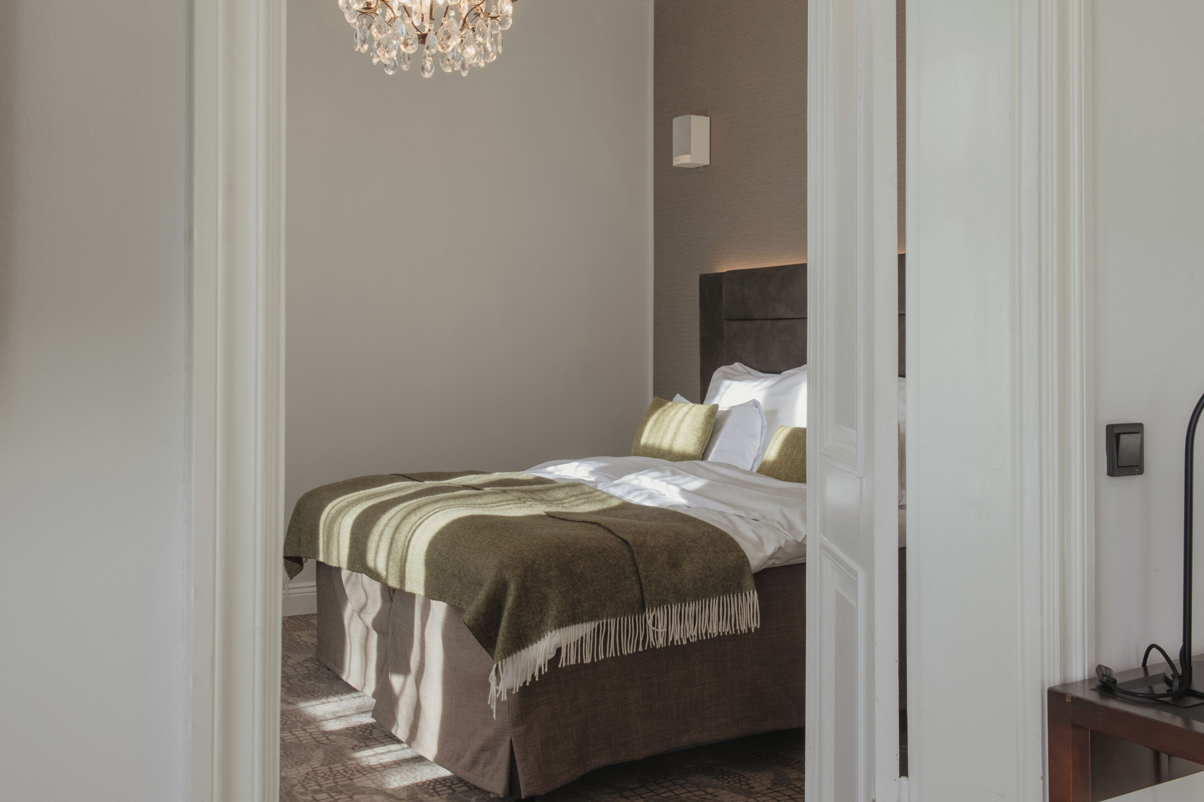 A bedroom with a bed, a chandelier, and a bedside table.