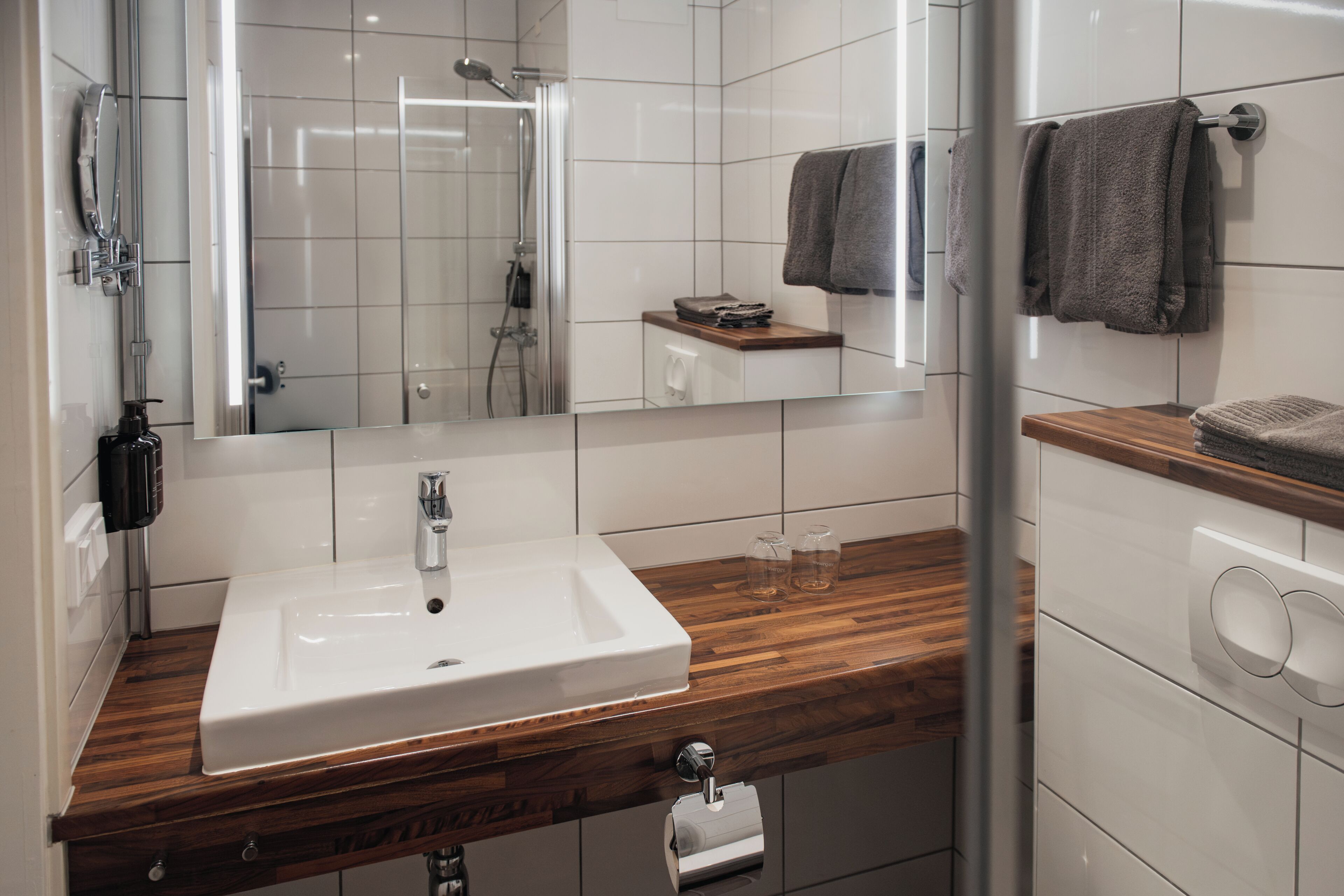 A modern bathroom with a white sink, wooden countertop, and a glass shower enclosure.