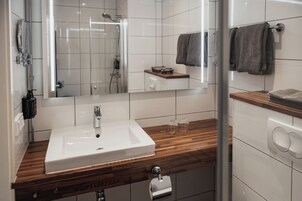 Un baño moderno con lavamanos blanco, encimera de madera y cabina de ducha de vidrio.