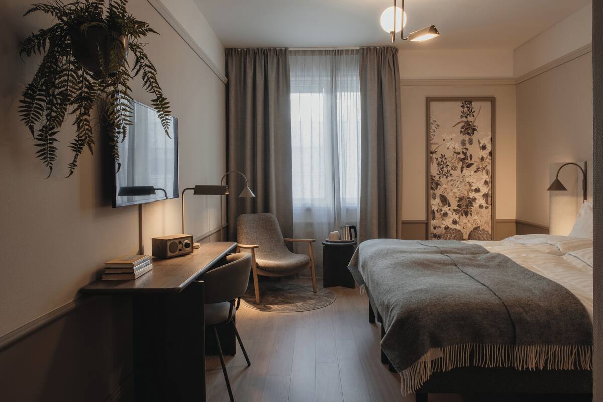 Hotellihuone, jossa on sänky, työpöytä, tuoli, televisio ja ruukussa oleva kasvi.