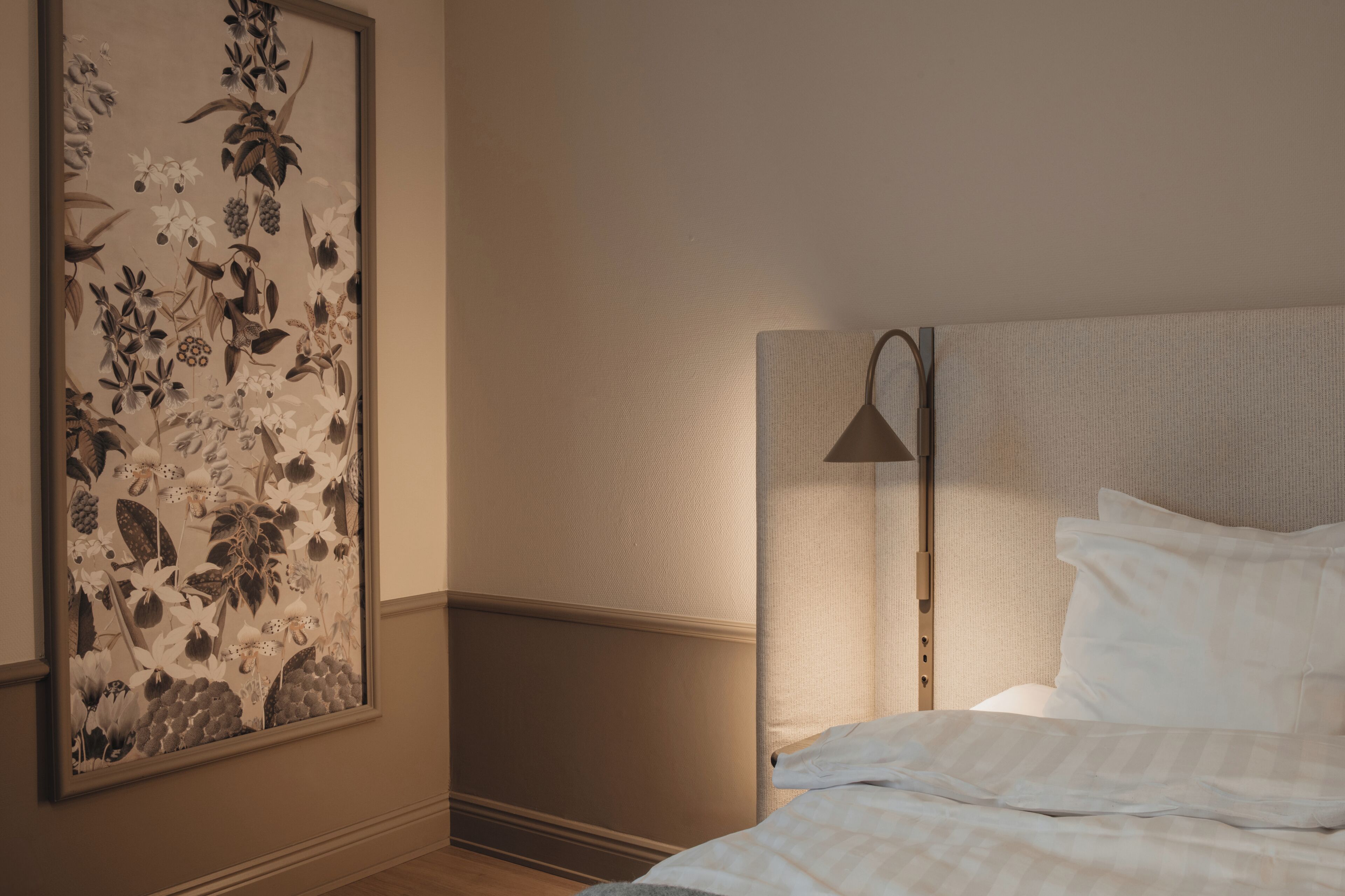 Un dormitorio con una cama, una mesita de noche, una lámpara y una obra de arte floral en la pared.