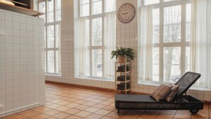 A room with large windows, a clock, a wicker lounge chair, and a shelf with folded towels.