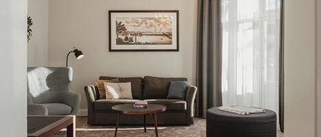 A living room with a sofa, a round coffee table, a chair, a round ottoman, a framed picture on the wall, and a chandelier.