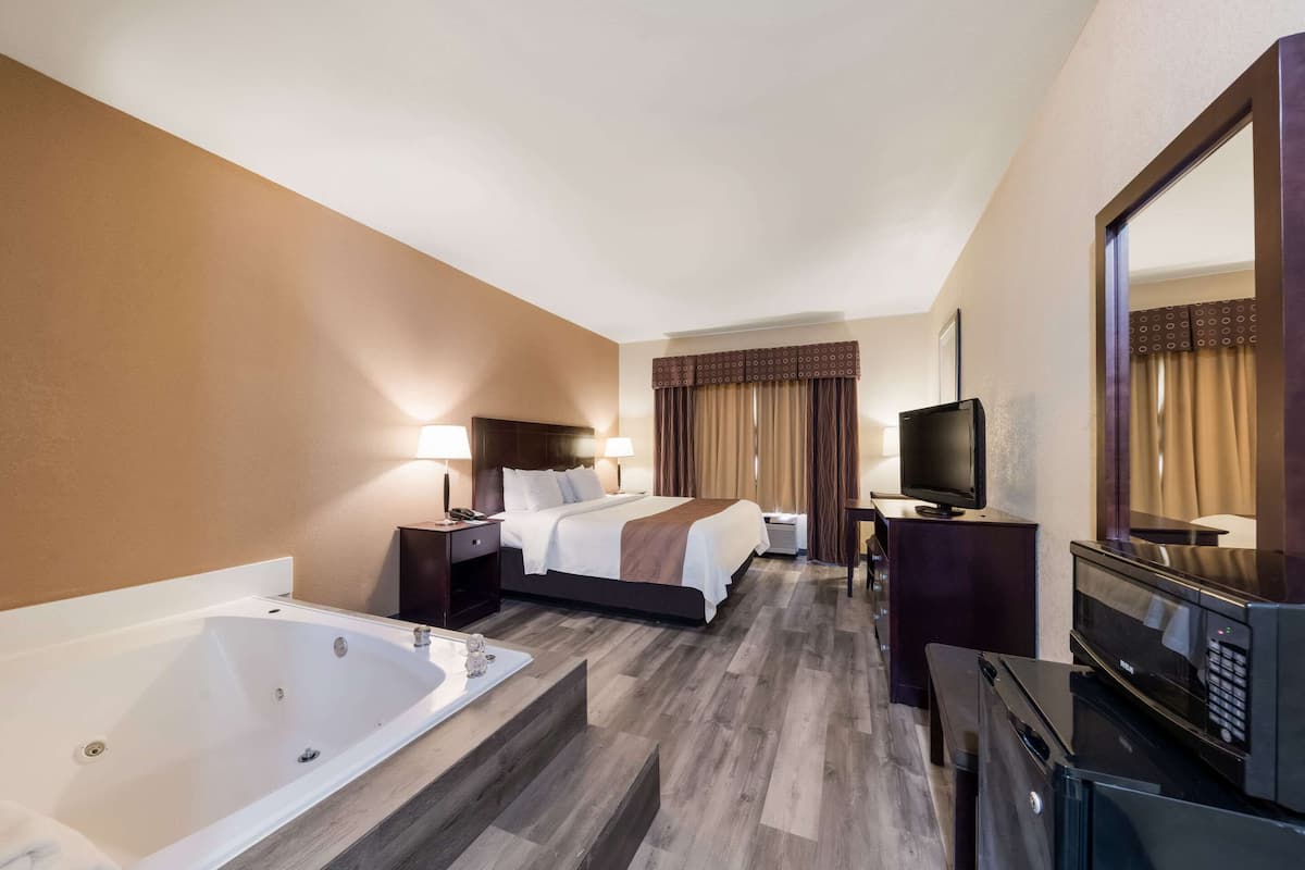 A hotel room with a large bed, a separate bathroom with a bathtub, a flat-screen TV, and a microwave.
