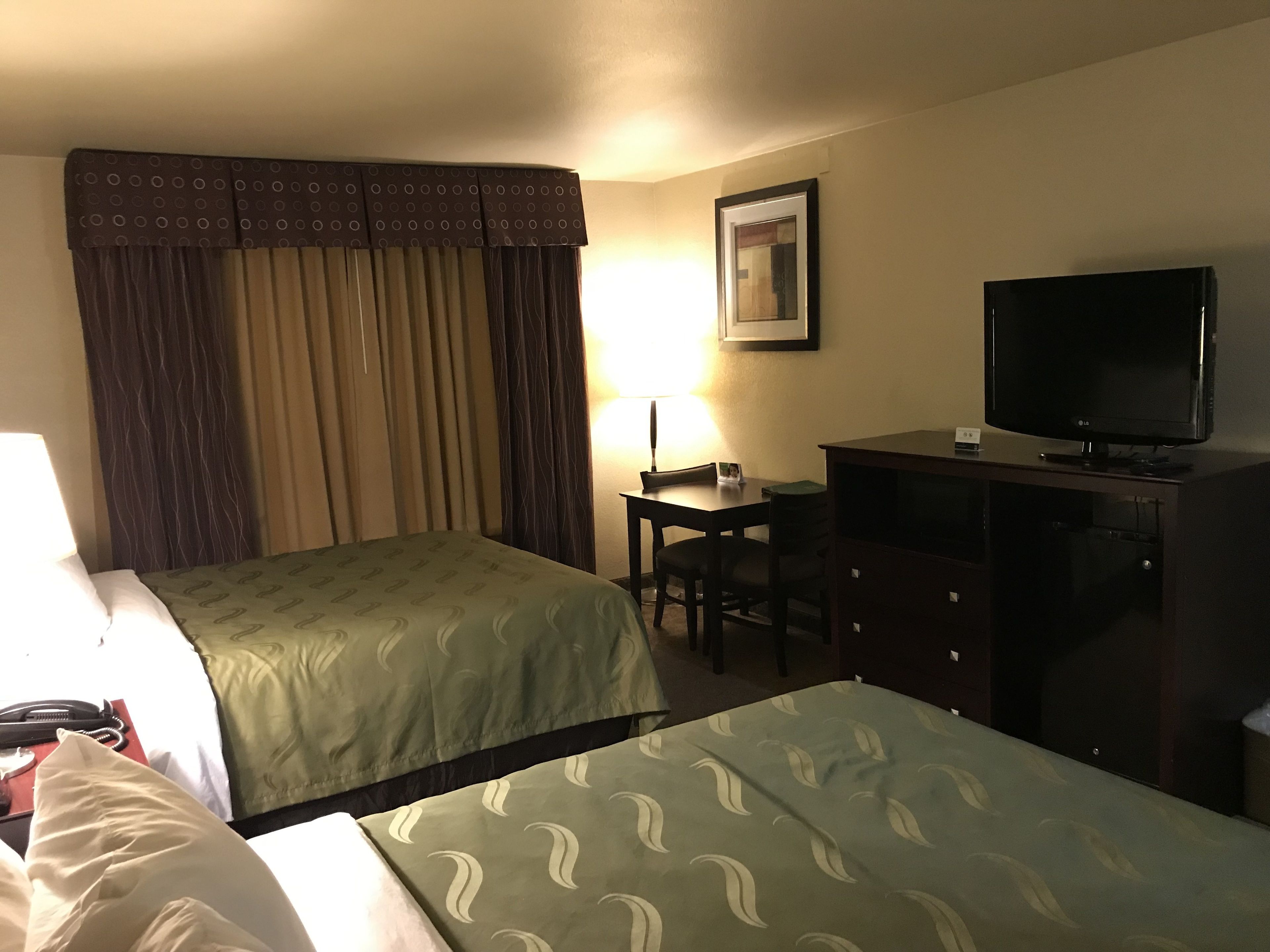Una habitación de hotel con dos camas, un escritorio, un televisor y una lámpara.