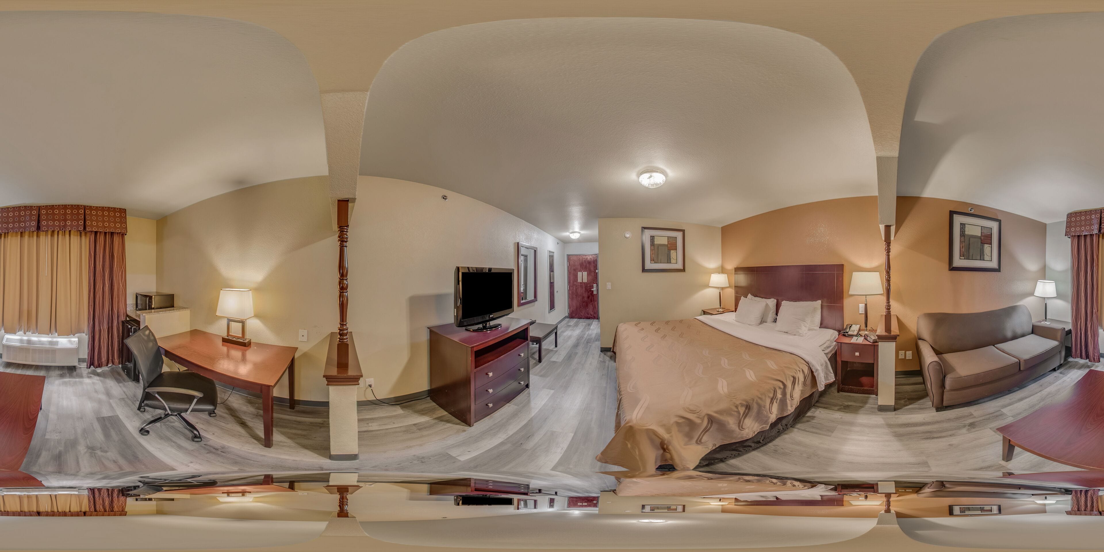 A panoramic view of a hotel room with a desk, chair, TV, bed, and nightstands.