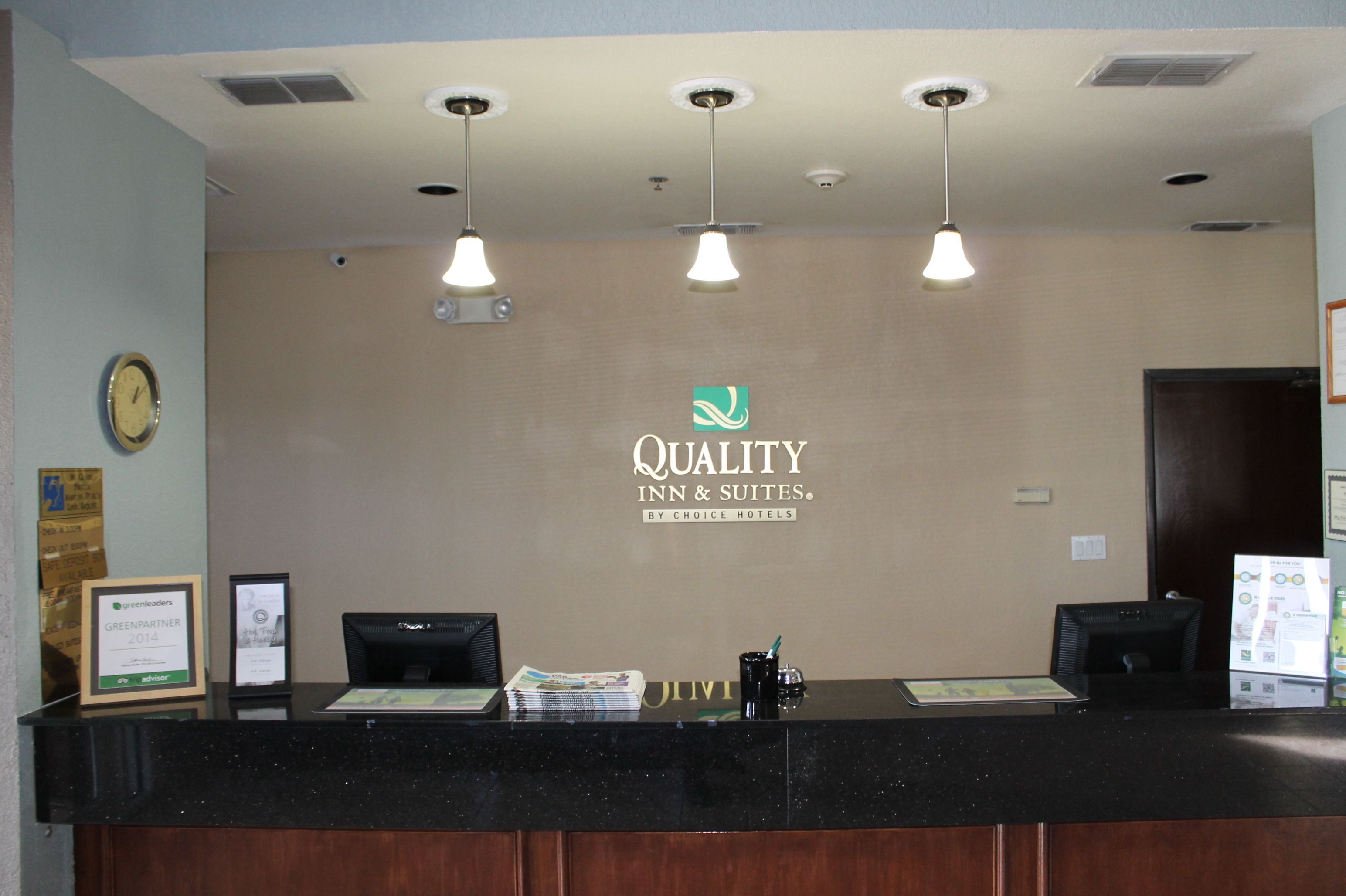 A hotel reception desk with a logo, a clock, and a framed certificate.