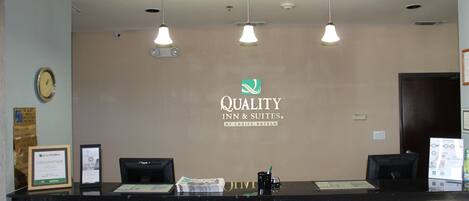 A hotel reception desk with a logo, a clock, and a framed certificate.