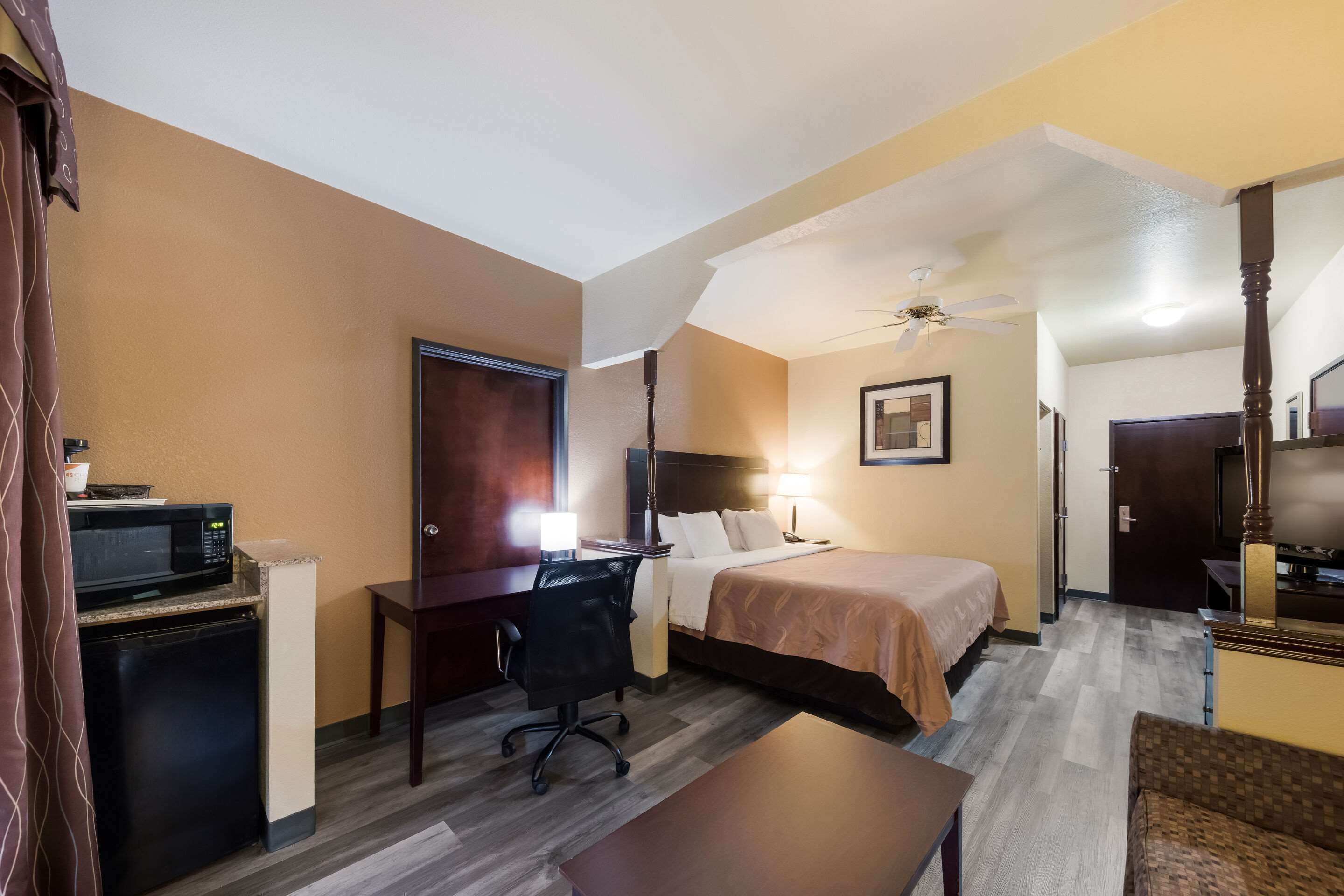 A hotel room with a bed, desk, chair, microwave, and a ceiling fan.