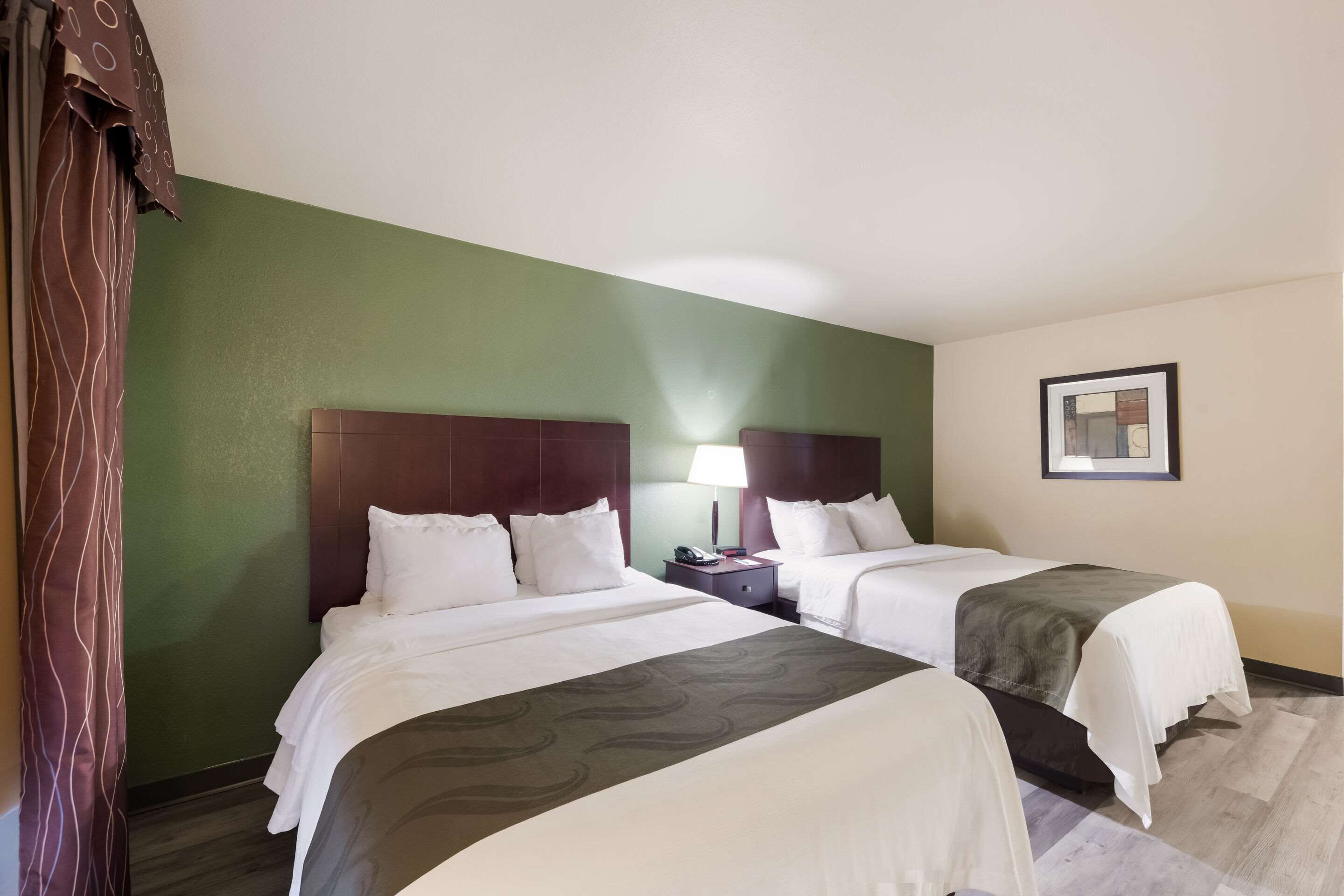 A hotel room with two beds, a nightstand with a lamp, and a framed picture on the wall.