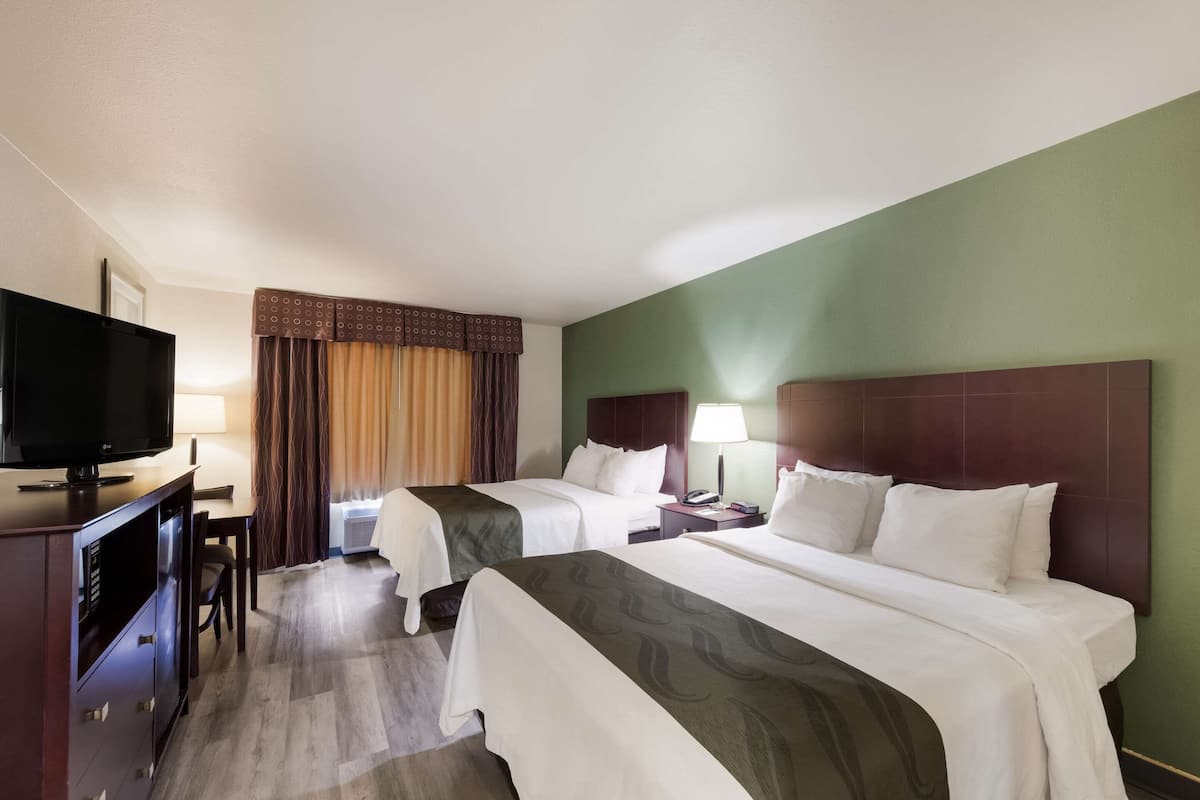 A hotel room with two beds, a TV, a desk, and a lamp.