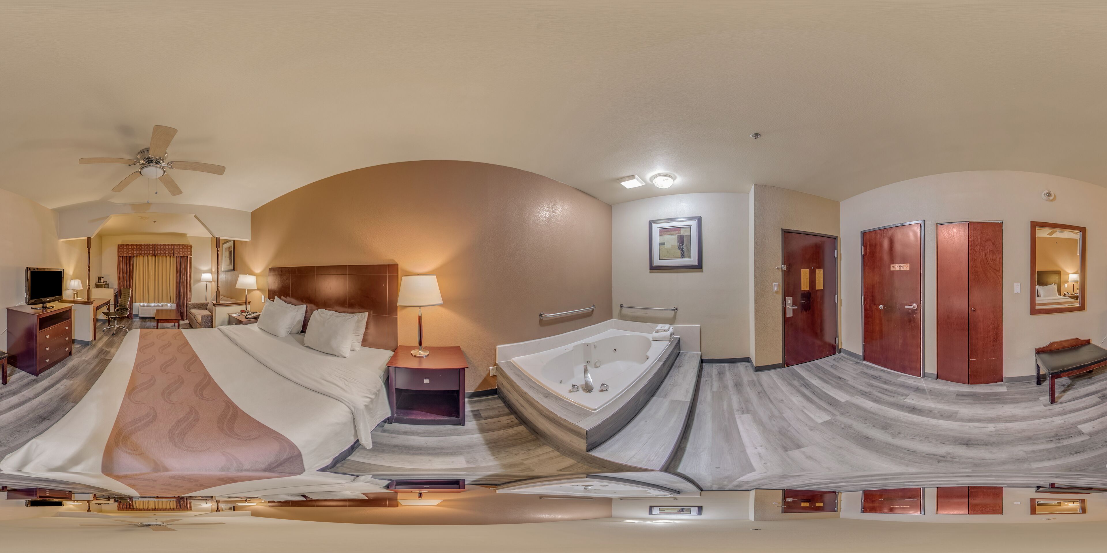 A hotel room with a large bed, a separate bathroom, a desk, and a ceiling fan.