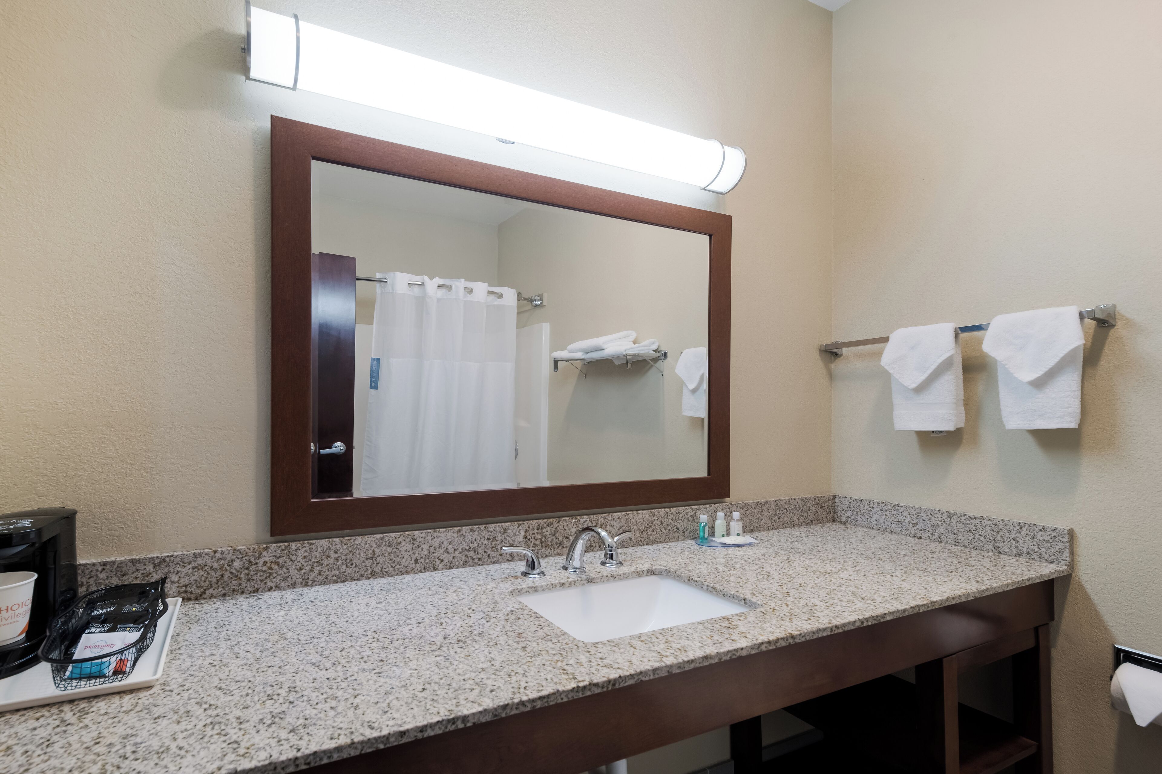 Un baño de hotel con lavamanos de encimera de granito, un espejo grande y un perchero con dos toallas.