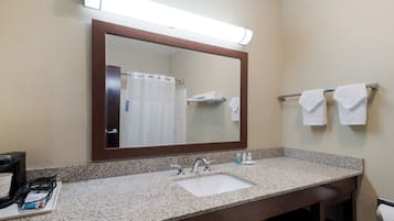 Un baño de hotel con lavamanos de encimera de granito, un espejo grande y un perchero con dos toallas.