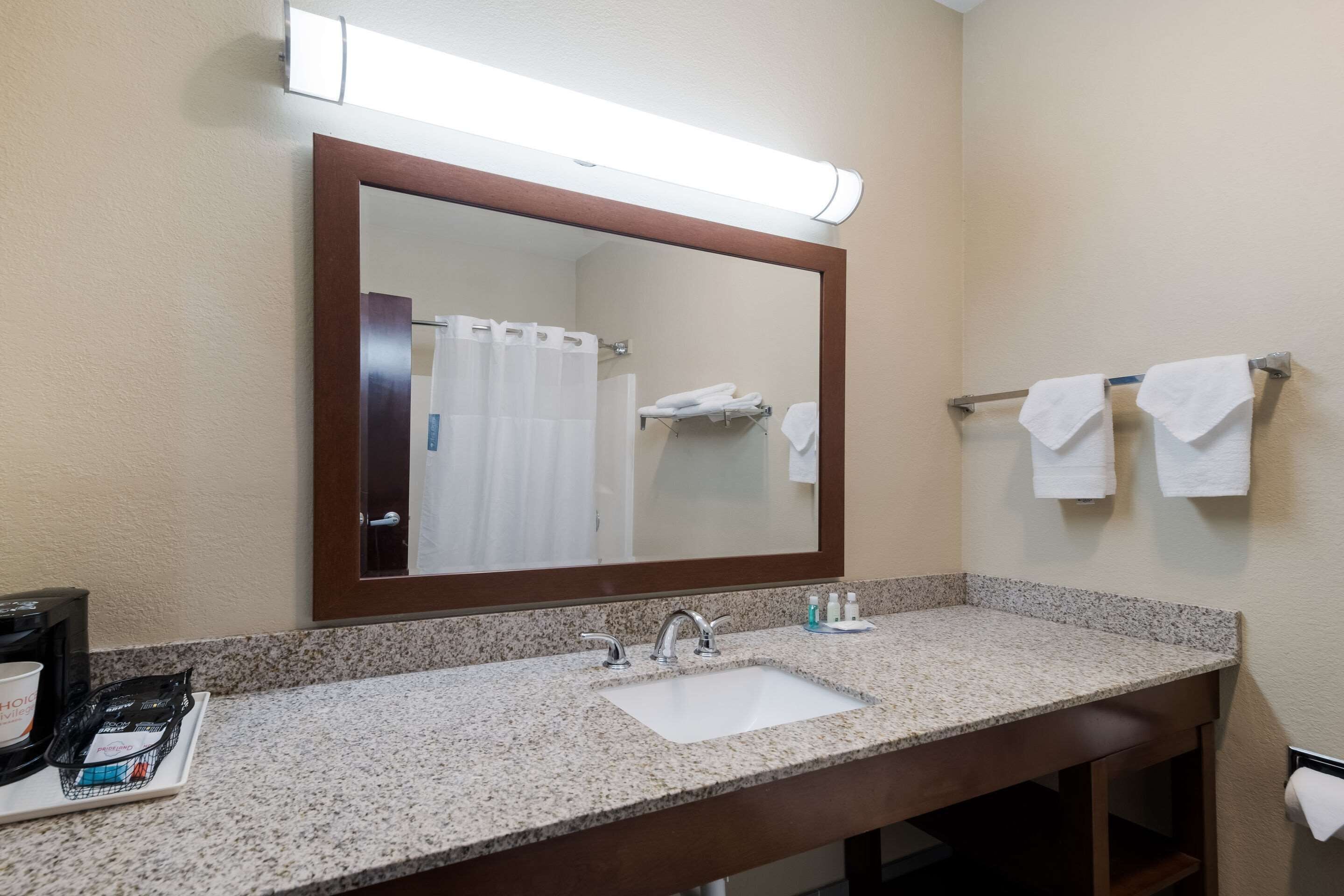 Un baño de hotel con lavamanos de encimera de granito, un espejo grande y un perchero con dos toallas.