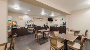 Un restaurante con mesas y sillas de madera, una zona de cocina y un televisor en la pared.