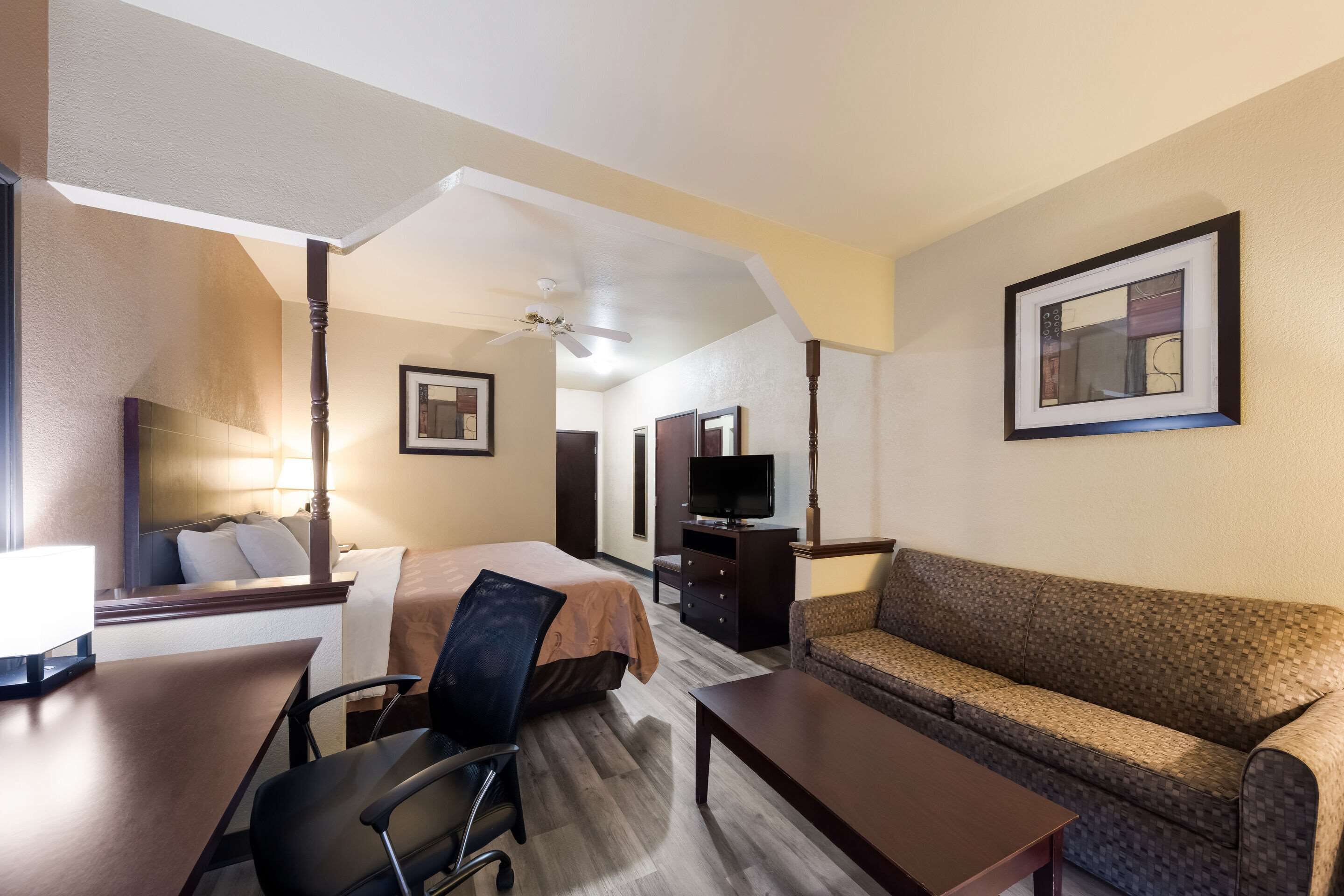 Ein Hotelzimmer mit Bett, Sofa, Schreibtisch mit Stuhl, Fernseher und einem gerahmten Bild an der Wand.