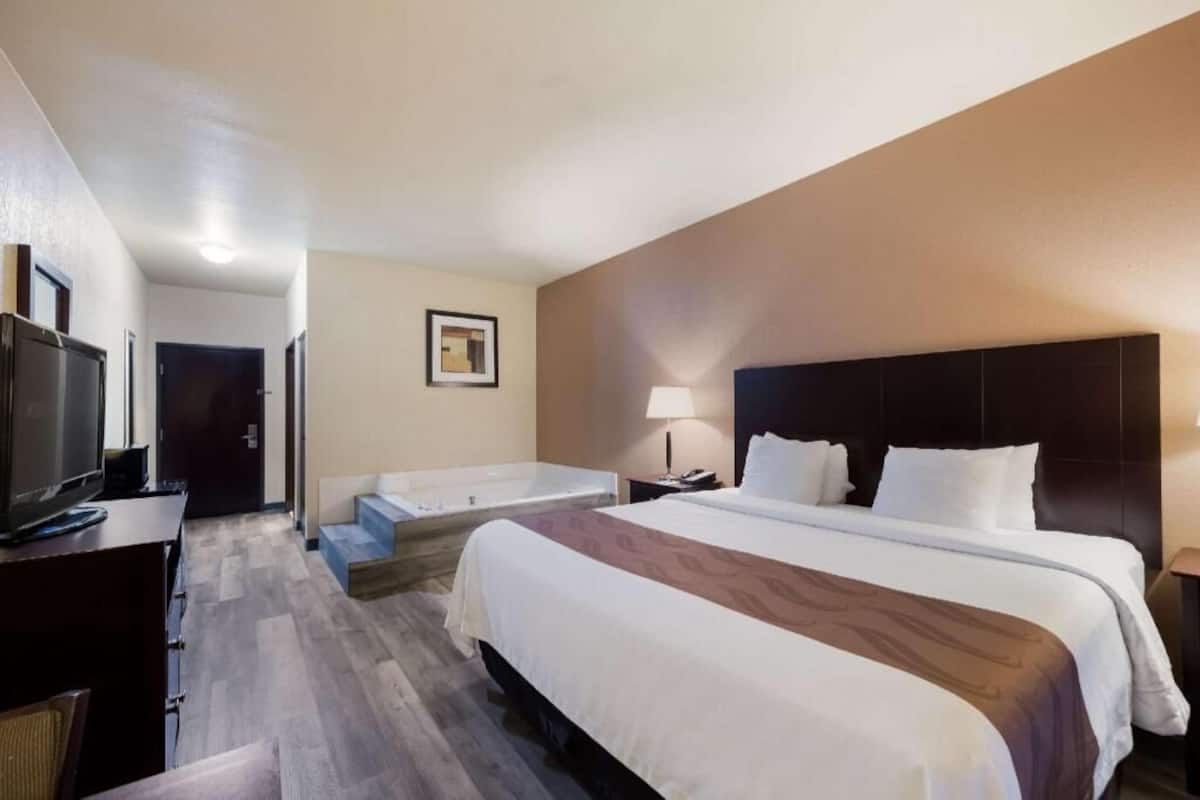 A hotel room with a large bed, a desk with a TV, a small seating area, and a bathroom with a bathtub.
