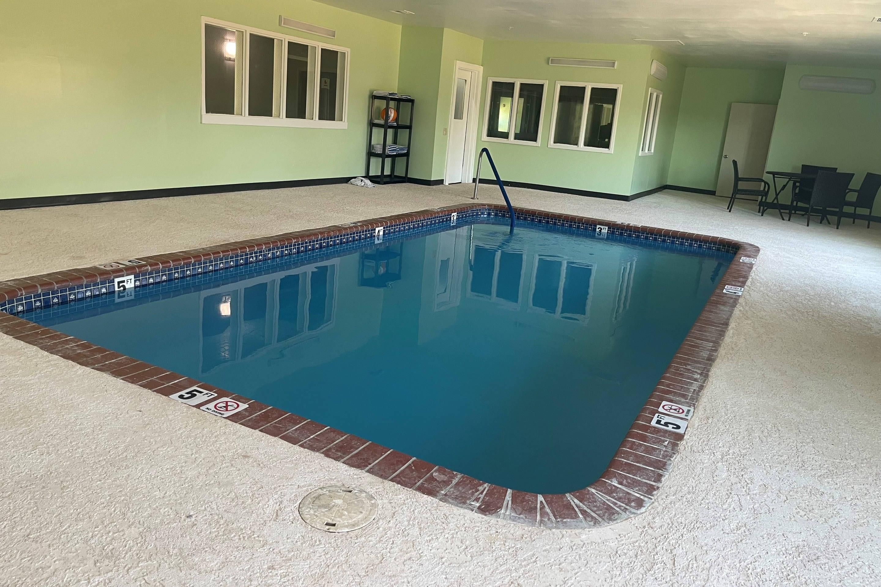 Una piscina rectangular interior con borde de azulejos, una escalera y una puerta que da a otra habitación.