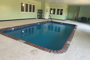 A rectangular indoor pool with a tiled edge, a ladder, and a door leading to another room.
