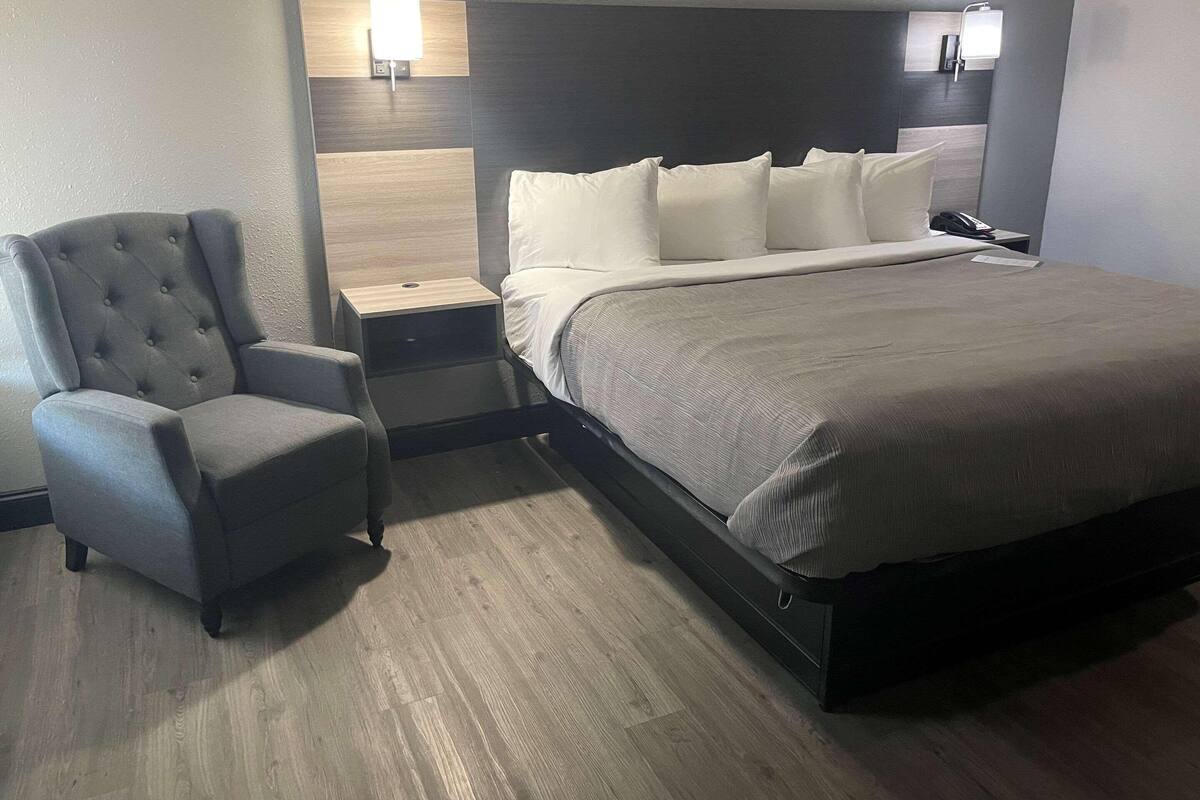 A hotel room with a bed, a chair, a nightstand, and a wall-mounted light.