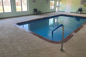 An indoor swimming pool with a blue tiled edge, a blue pool ladder, and a carpeted floor. - Quality Suites Abilene Mall Area (Abilene)