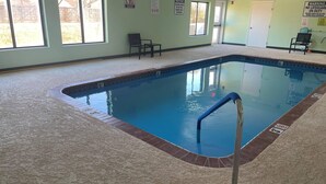 An indoor swimming pool with a blue tiled edge, a blue pool ladder, and a carpeted floor. - Quality Suites Abilene Mall Area (Abilene)