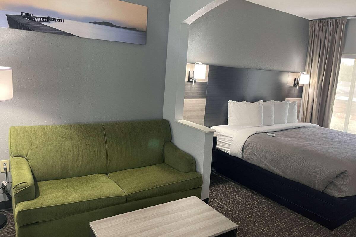 A hotel room with a green sofa, a bed with white bedding, a small table, and a painting on the wall.