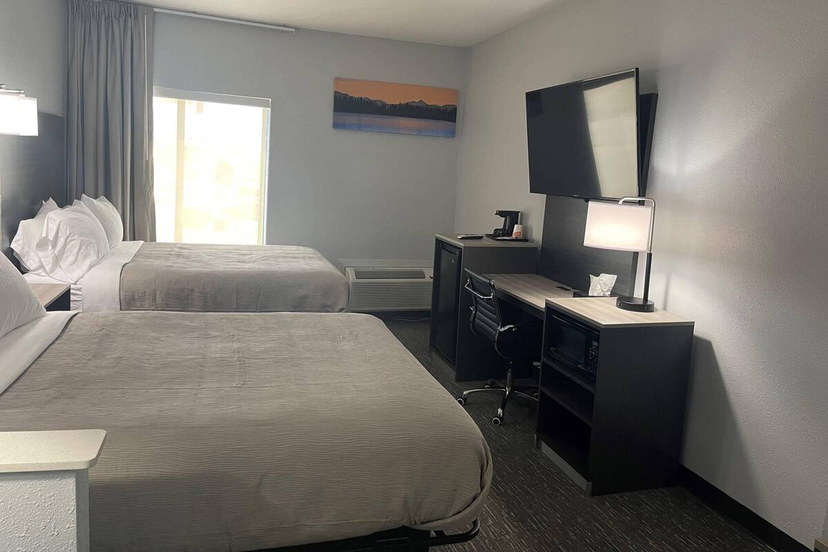 A hotel room with two beds, a desk with a computer, a TV, and a painting on the wall.