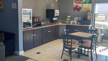 A modern kitchen with a dining area, equipped with a coffee machine, a refrigerator, and a window with a view.