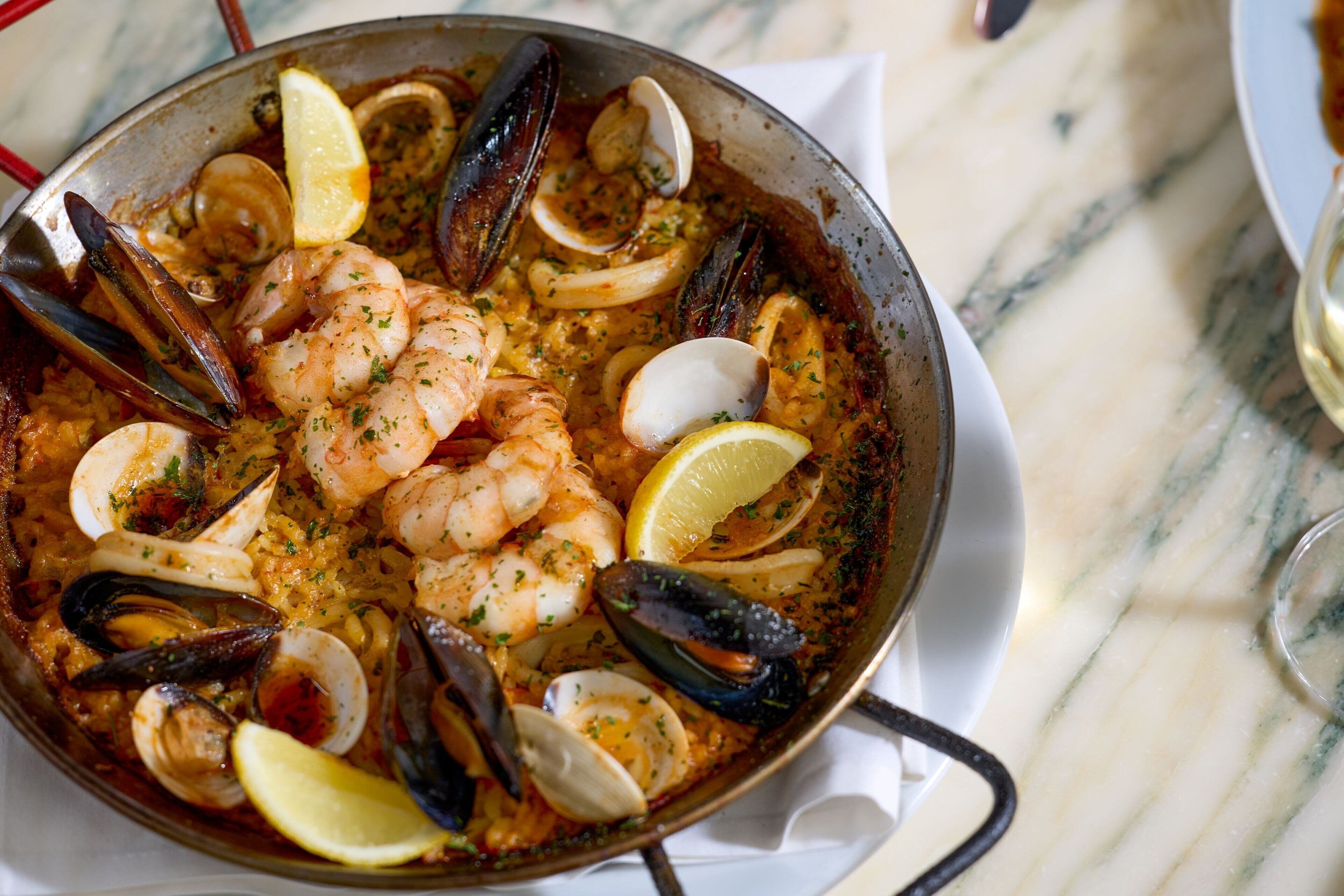 A seafood paella dish with shrimp, mussels, clams, and lemon slices.