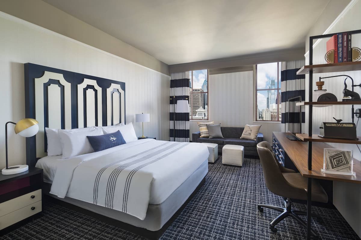 Une chambre d’hôtel avec un grand lit, un bureau, une chaise, une bibliothèque et une vue sur le paysage urbain.
