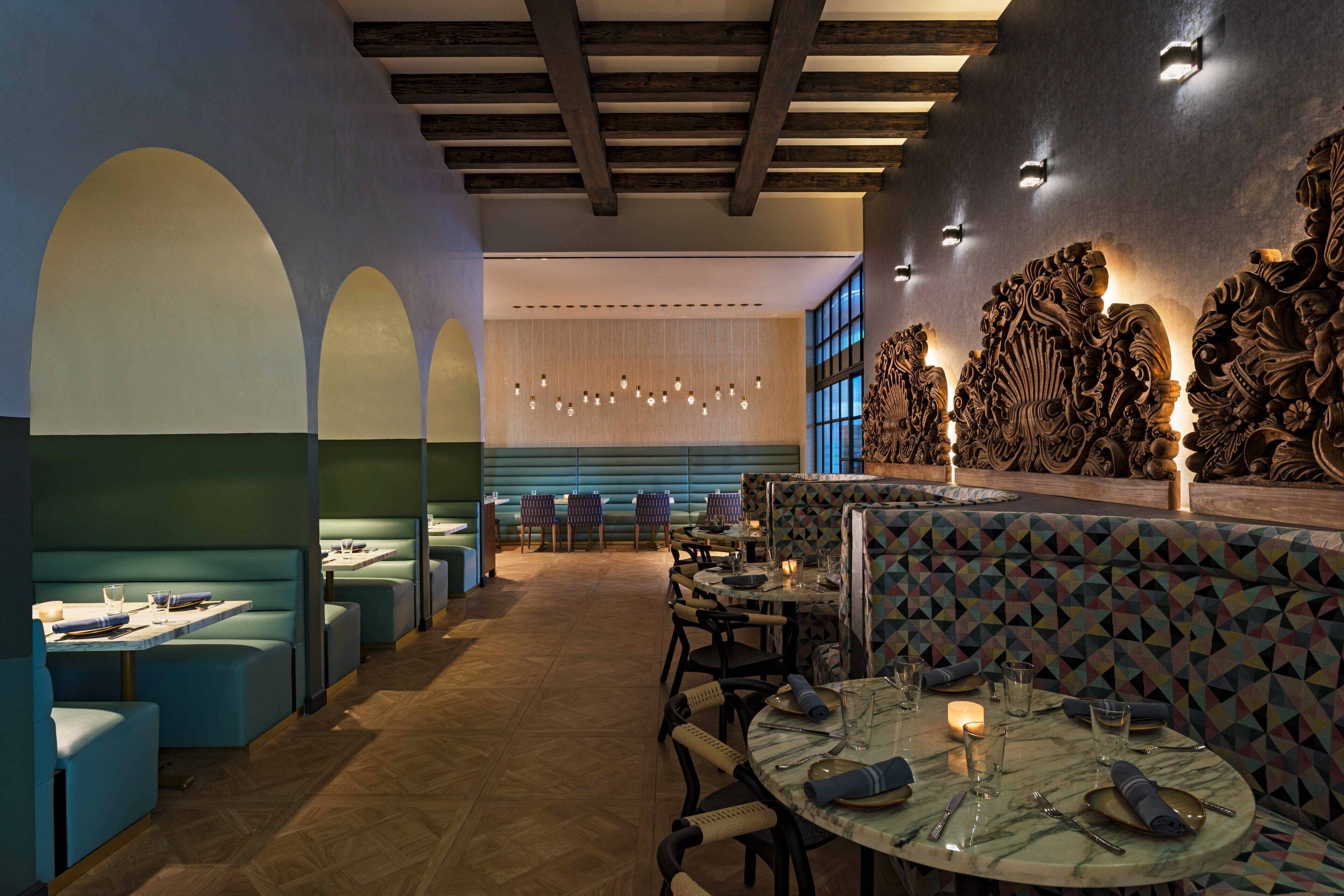A restaurant with booths and round tables, wooden beams on the ceiling, and a patterned wall.