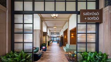 A spacious hallway with a sign reading "sabrós + sorbō" leading to a seating area with sofas and potted plants.