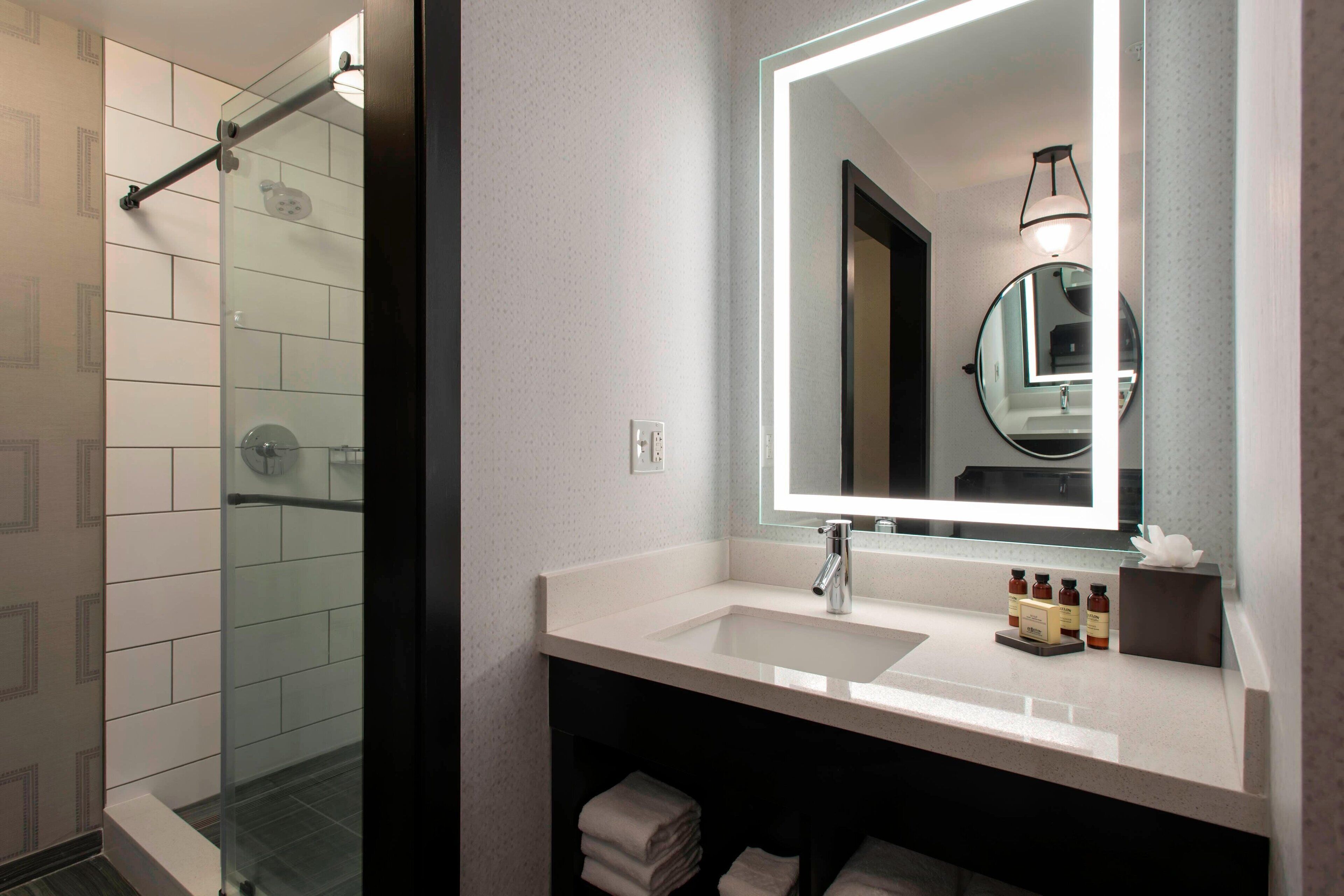 A modern bathroom with a glass shower enclosure, a white sink with a mirror, and neatly folded towels.