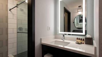 A modern bathroom with a glass shower enclosure, a white sink with a mirror, and neatly folded towels.