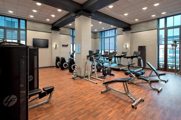 A gym with exercise equipment, large windows, and a wooden floor.