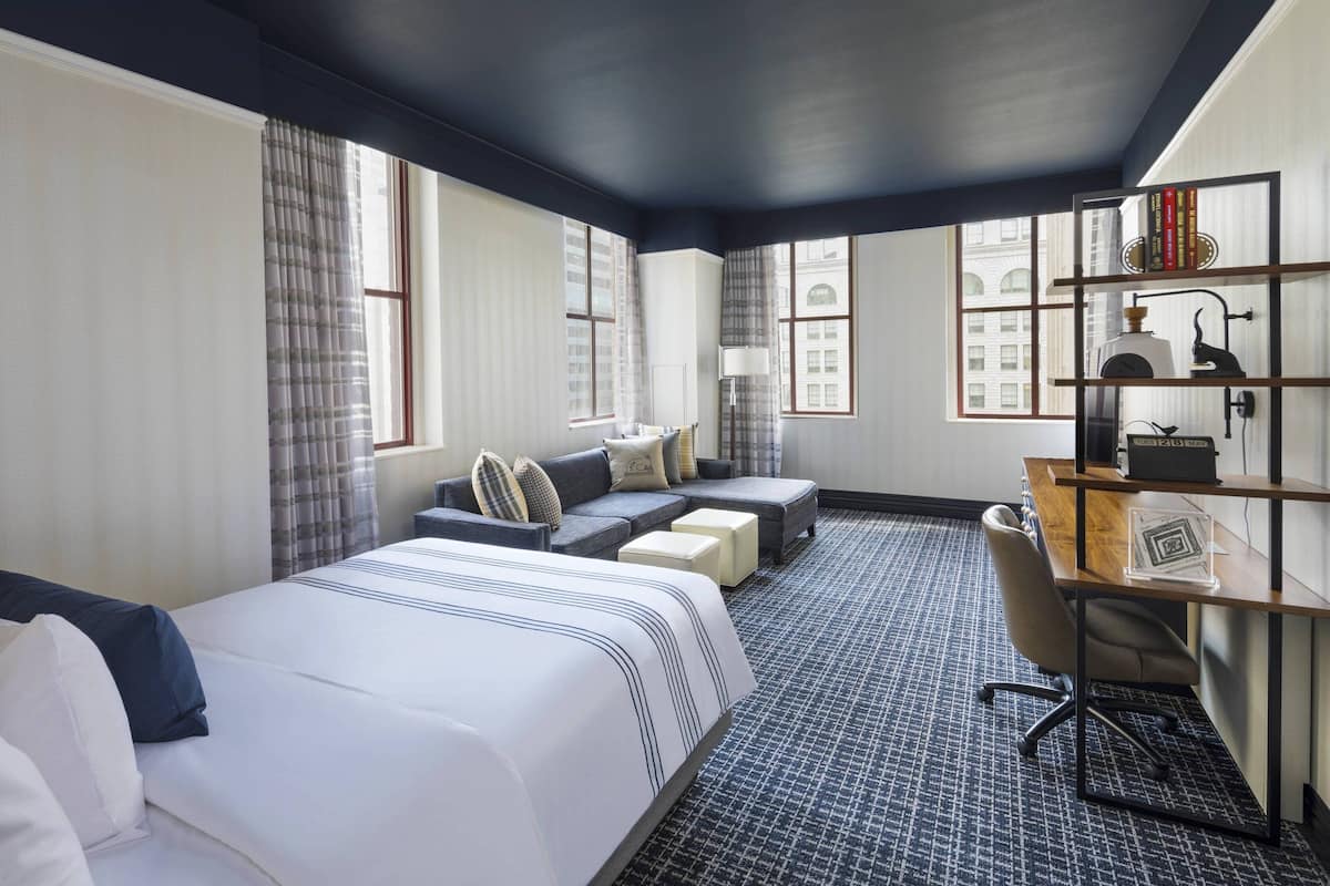 Une chambre d’hôtel avec un grand lit, un canapé, un bureau et une bibliothèque.