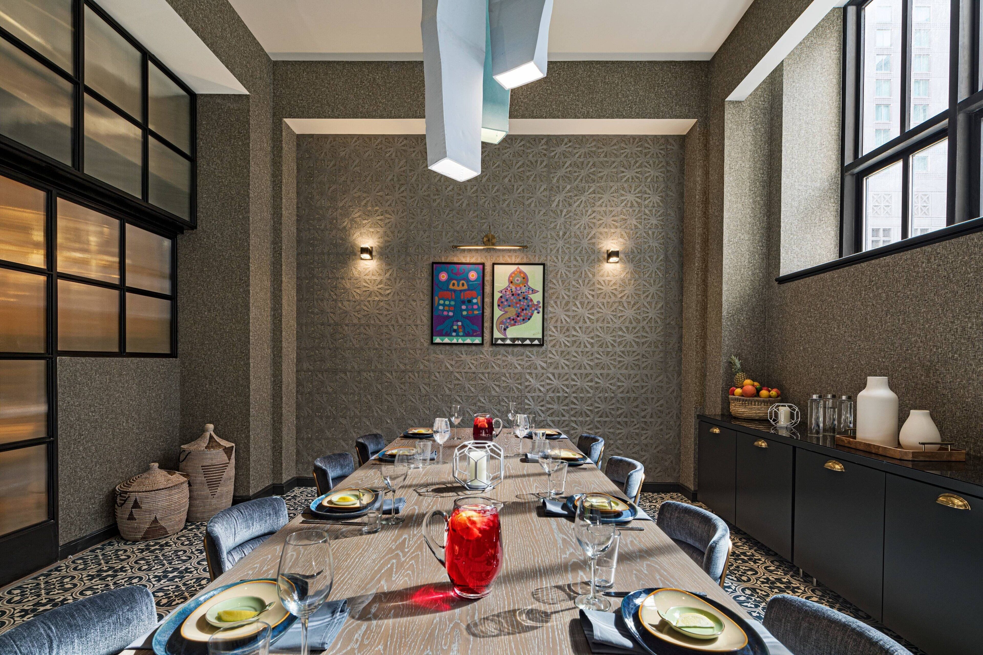 A dining area with a long table set for six, featuring a patterned tablecloth, modern chairs, and a central decorative pitcher.