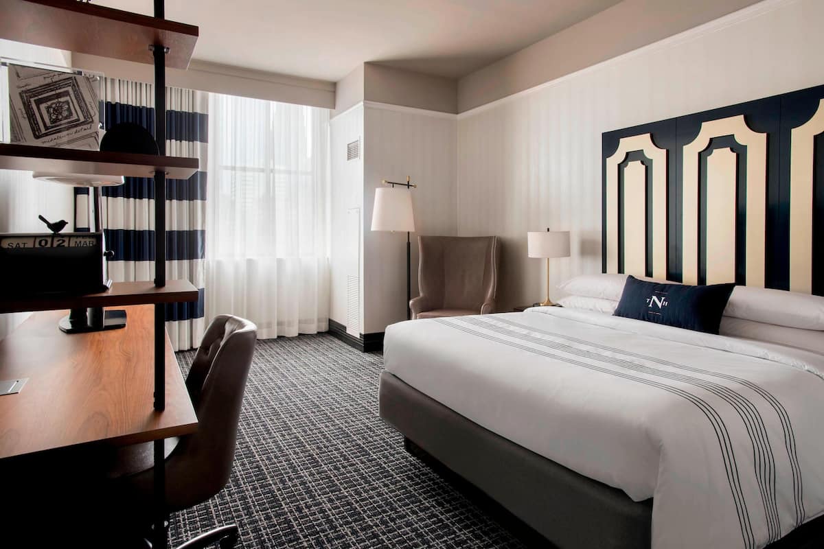 Une chambre d’hôtel avec un grand lit, un bureau équipé d’un ordinateur, une chaise et une lampe.