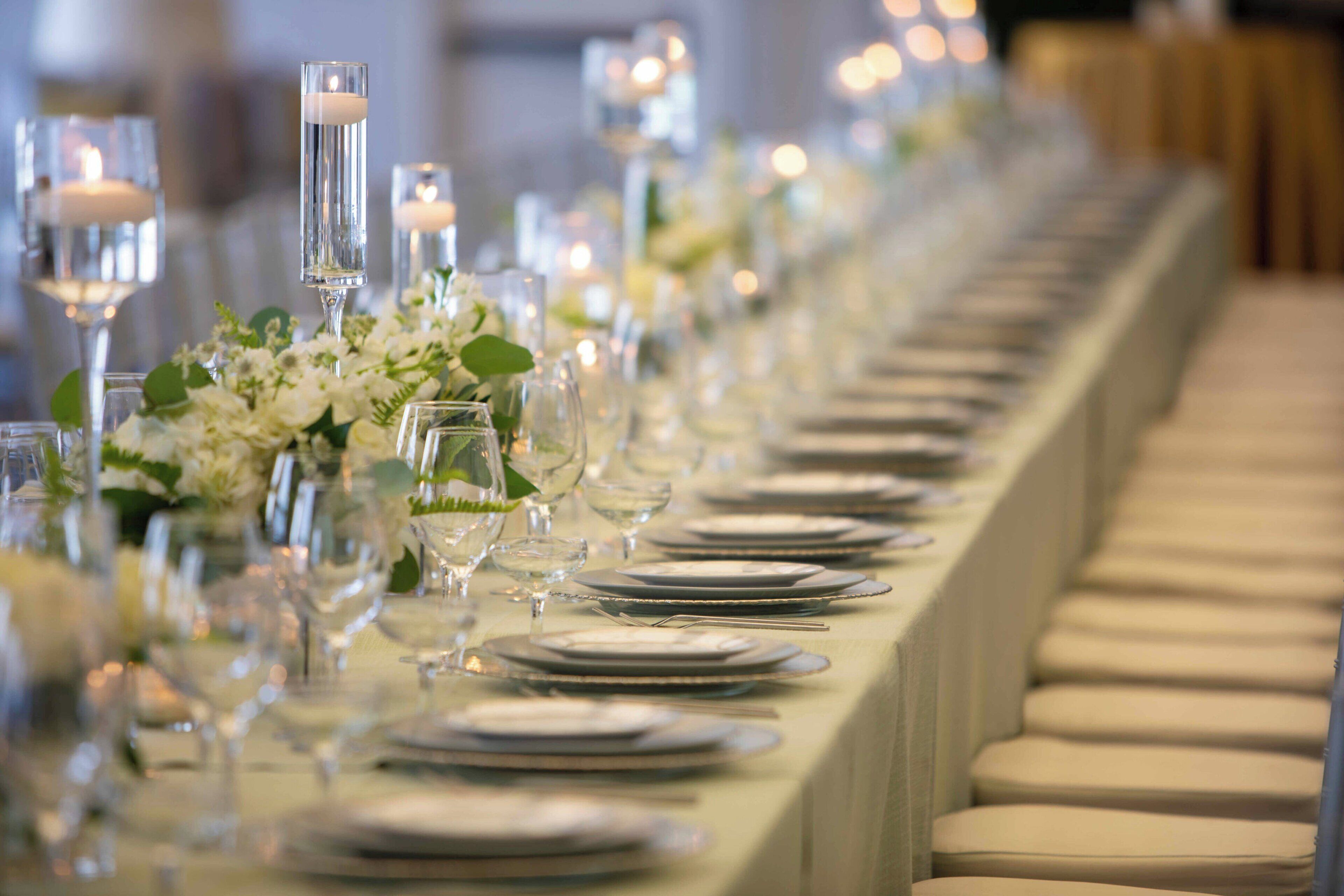 A long table set with plates, glasses, and candles, suggesting a formal dining setting.