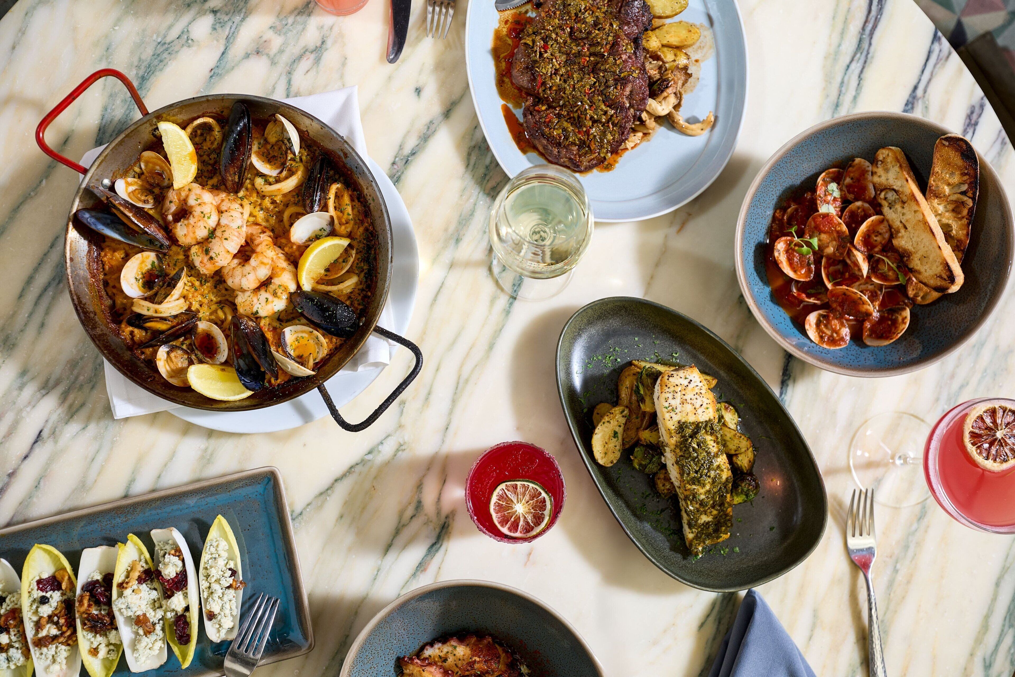 Variedad de platos sobre una mesa de mármol, incluyendo mariscos, un bistec y un bol de pasta.