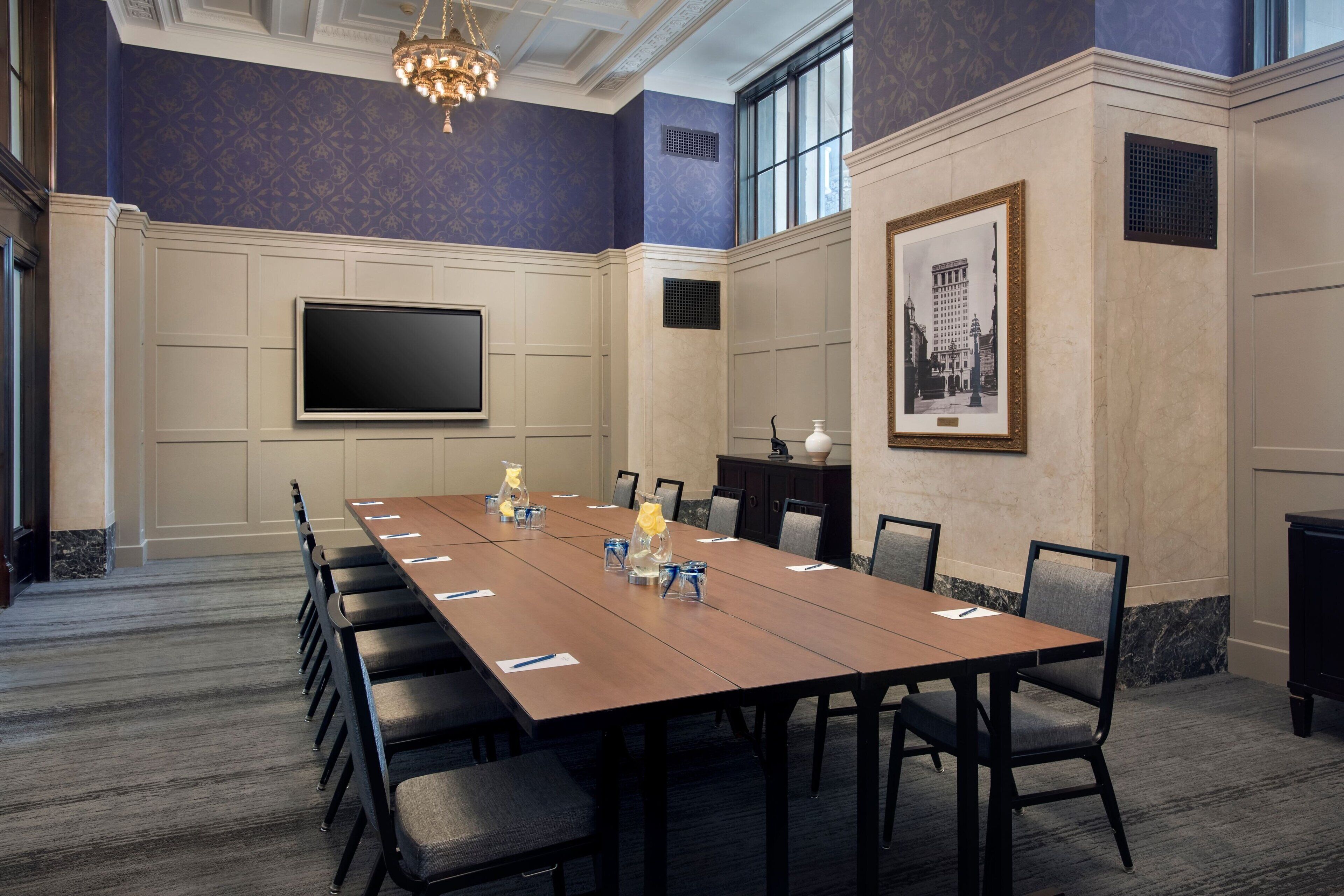 A conference room with a long table, chairs, a flat-screen TV, and a framed picture on the wall.