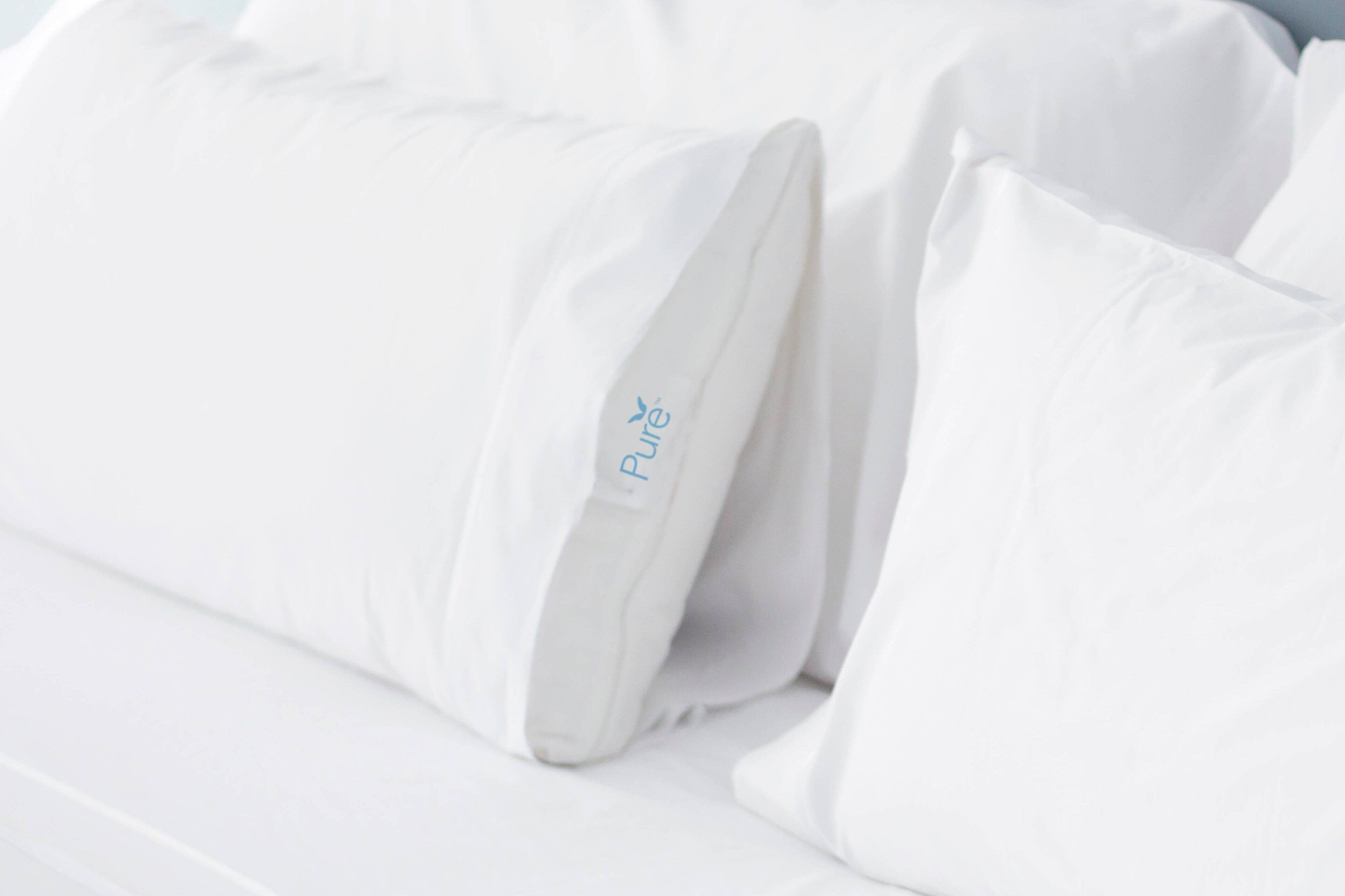 A white pillow with a small blue logo on a bed.