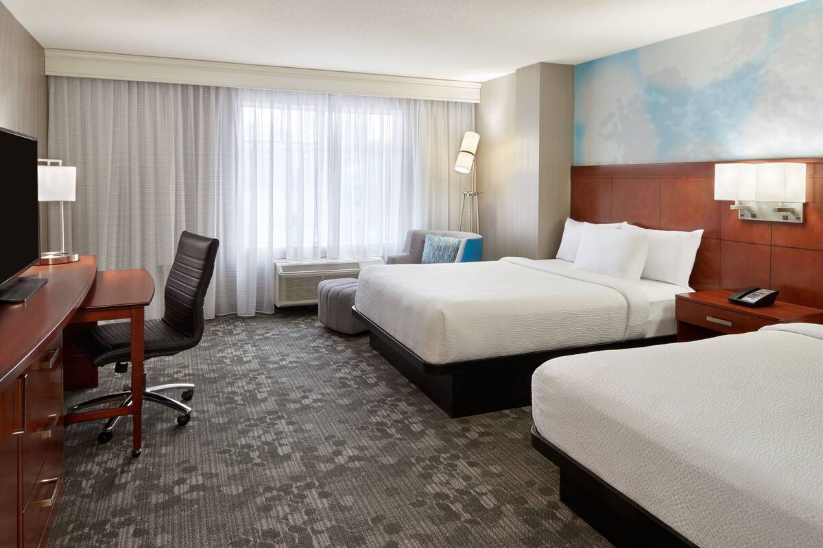 Habitación de hotel con una cama grande, un escritorio con silla, un televisor y una ventana con cortinas.