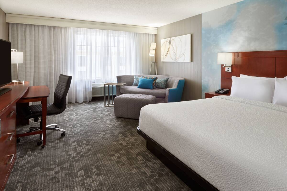 Habitación de hotel con una cama grande, un escritorio con silla, un sofá, una mesita y una lámpara.