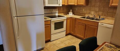 Una cocina compacta con armarios de madera, un refrigerador, un microondas, un horno y un lavavajillas.