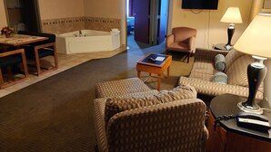 Hotellihuone, jossa on oleskelualue, ruokapöytä, sohva, tuoli, televisio, lamppu ja kylpyamme.